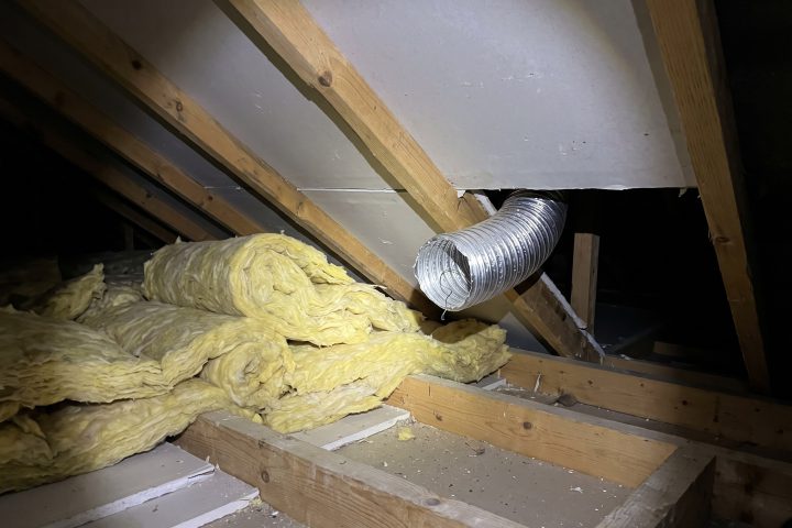 Loft insulation rolled back from the eaves with an unconnected extractor duct
